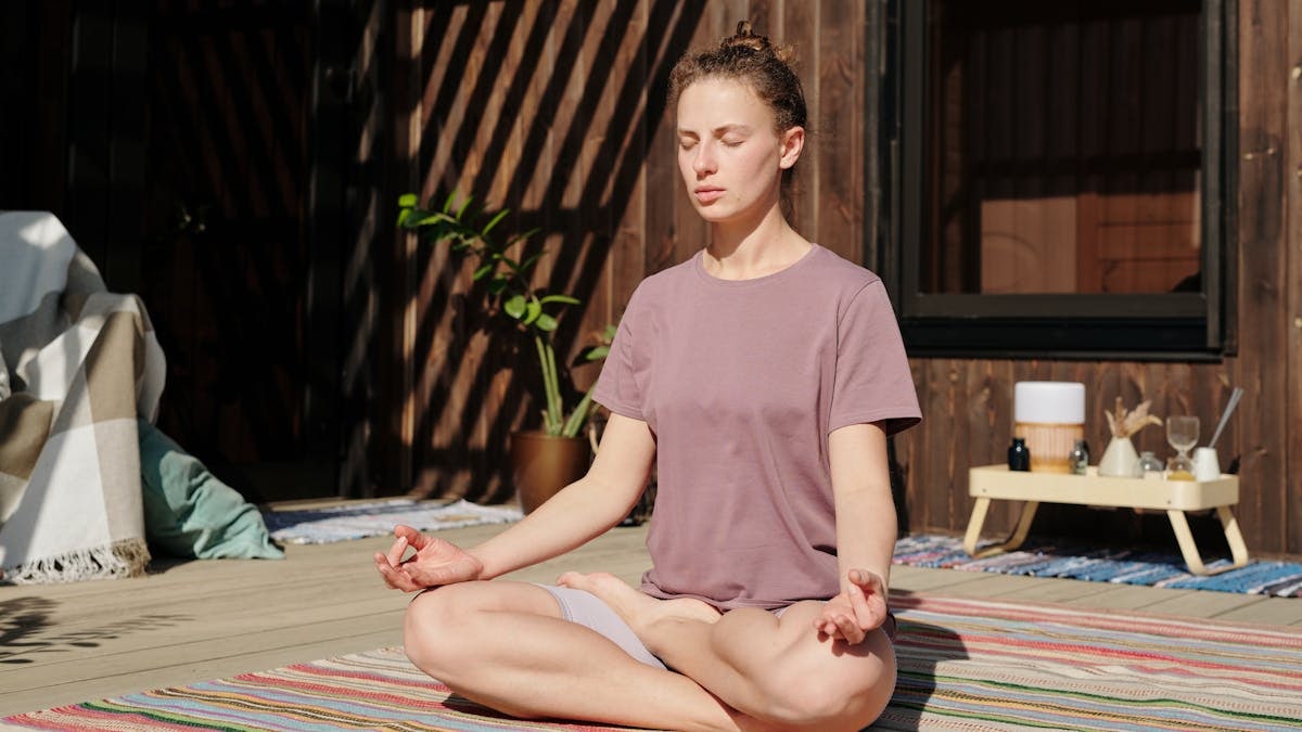 Woman practicing meditation in lotus pose on a sunny outdoor deck.